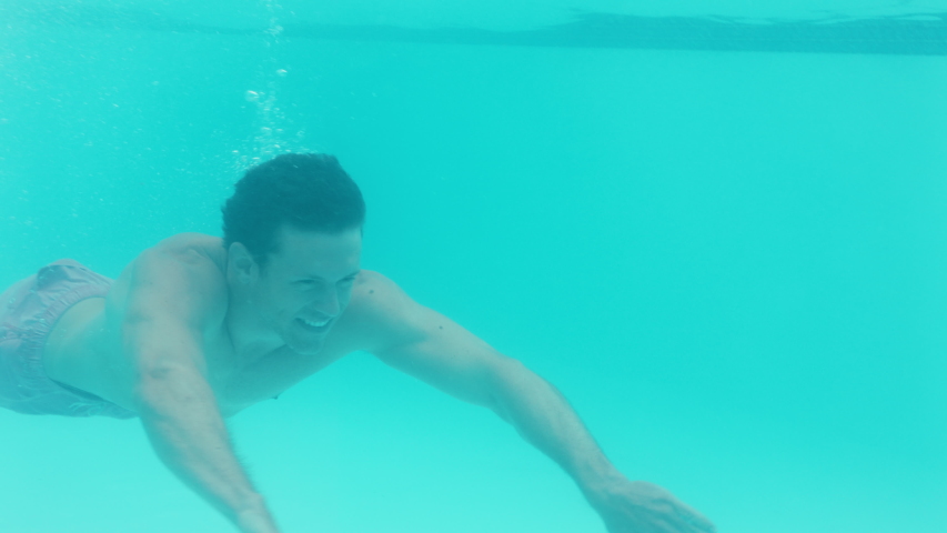 attractive young man swimming underwater in pool waving hand smiling happy floating in crystal clear water having fun swim in summertime 4k