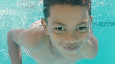 happy little boy swimming underwater in pool smiling enjoying swim in crystal clear water on summer day 4k