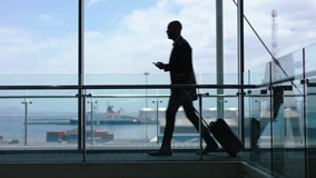 businessman walking with trolley bag using smartphone traveling for international business trip in airport lobby with view of harbor port 4k footage - Powered by Shutterstock - Get 15% off with code: PIKWIZARD15