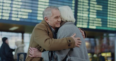 Caucasian old happy couple meeting and hugging at the airport terminal after one of them arrival. Indoor.