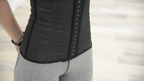 Girl in gray sports leggings unbutton a black corset