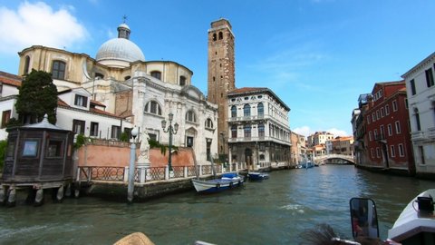 Venice / Italy - June 23, 2019: BOAT TRAVEL: San Geremia church dome with ancient Romanesque bell tower and Palazzo Labia on Grand Canal Venice Italy with blue sky.