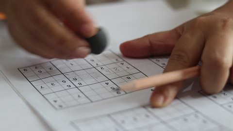 Solve sudoku puzzle with pencil as hobby by senior woman on wooden office desk. Player insert numbers into grid consisting of nine squares subdivided into further nine smaller squares.