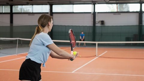 Young woman in sportswear and long hair making wide serve ball in tennis. Medium shot of female tennis player serving. Young people playing tennis in slow motion