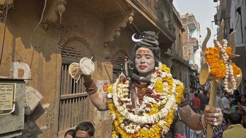 A man dressed as Lord Shiva sitting on a horse playing the damaru with his right hand and holding a Trident in his left hand and a crescent on his head. Varanasi, India (March 2019)