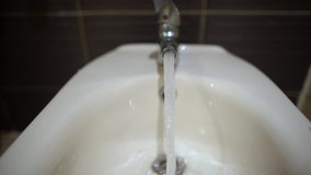 Slow motion video of running water in bidet at bathroom and female hand closes tap.