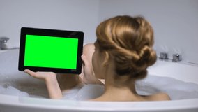 Woman in bath holding tablet PC, watching online video channel, back view
