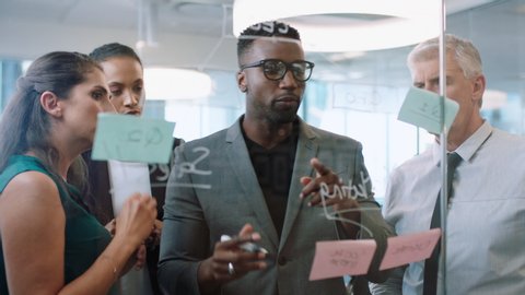 diverse business people using sticky notes african american team leader man brainstorming with colleagues working on solution discussing strategy writing on glass whiteboard in office meeting 4k