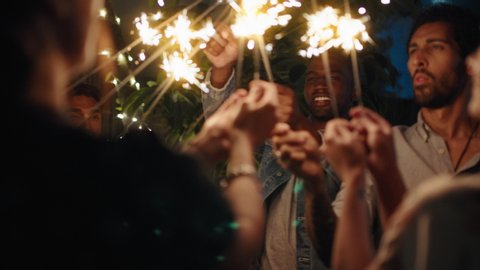new years eve friends celebrating with sparklers smiling enjoying celebration together sharing holiday fireworks on peaceful evening at home in backyard 4k