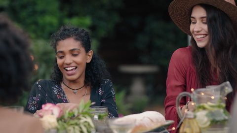 beautiful mixed race woman celebrating with friends enjoying dinner party chatting sharing healthy food sitting at table enjoying weekend reunion relaxing on beautiful summer evening outdoors
