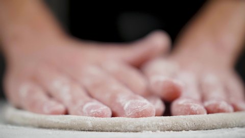 Cook prepares wheat dough for pizza on the black background