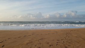 Slow video of Water waves in sea with horizon and blue sky with clouds and beach sand with human foot marks on it in day time