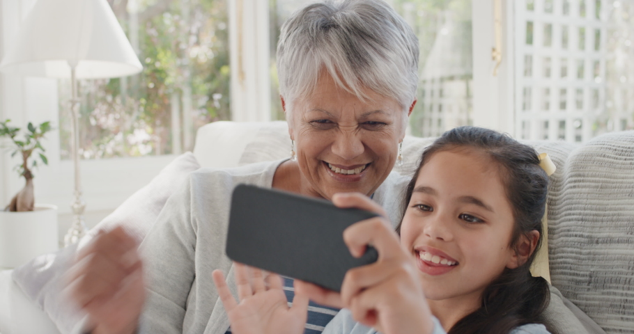 Happy girl using smartphone with granny having video chat waving at family sharing vacation weekend with grandmother chatting on mobile phone relaxing at home with granddaughter 4k | Shutterstock HD Video #1034557199