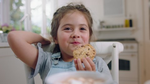 cute little girl eating cookie dipping biscuit into hot chocolate enjoying delicious treat at home in kitchen