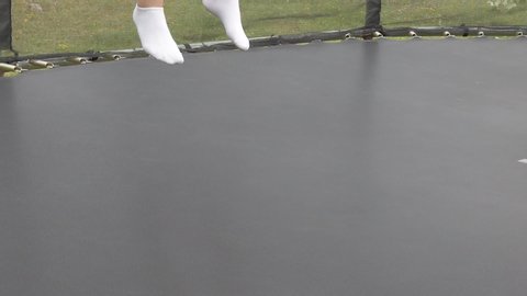 Small girl with short jeans, black t-shirt and white socks jumping on a black trampoline together with a young boy wearing green t-shirt, black shorts and black socks with white marked cross