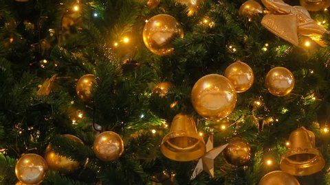 Close up a Christmas tree lights glittering at night. New Year fir tree with decorations and illumination. Xmas tree decorations background. Many large golden balls on fir tree New Year and Christmas