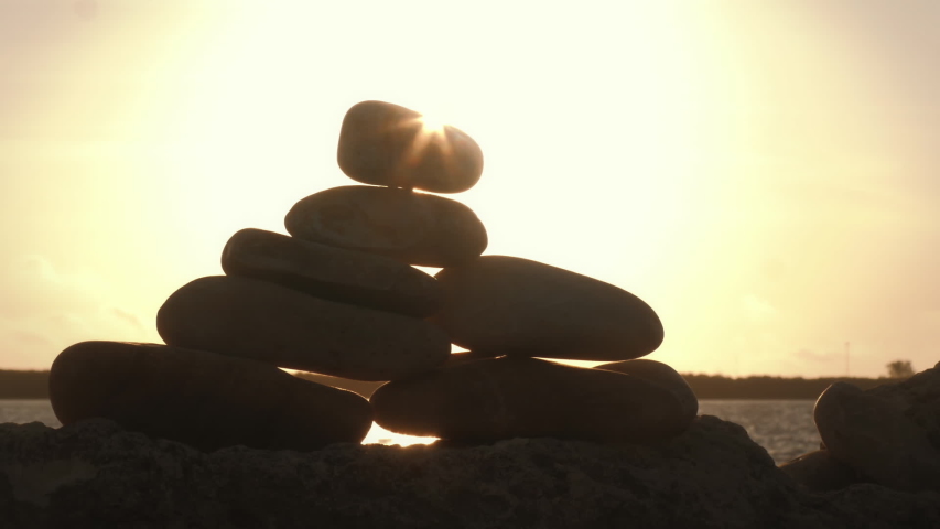 Hand balancing stack of rocks closeup in morning sun flare  | Shutterstock HD Video #1034574908