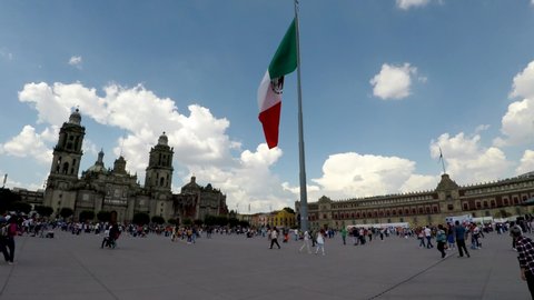 Mexico City, Mexico-July, 2019: View of the Mexican flag waving in the Plaza de la Constitución, many people visit the National Palace and the Metropolitan Cathedral.