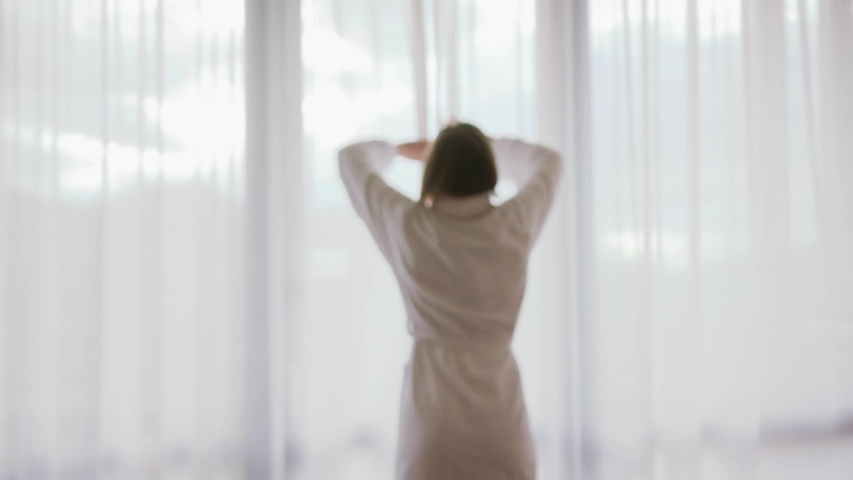 Close up back view young woman opening curtain lace standing in luxury apartment home or hotel looking through window enjoying wellbeing light city skyscrapers morning close up slow motion | Shutterstock HD Video #1034581406