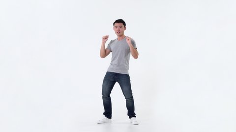 Full length portrait of happy excited young Asian man in casual gray t-shirt and jeans dancing over white background