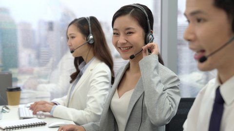 Beautiful Asian woman customer service operators talking on headsets and using computer at call center office with team