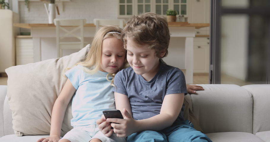 Two funny little kids siblings holding phone using smartphone playing mobile game browsing social media taking selfie at home having fun with cellphone device sit on sofa, children and gadget concept Royalty-Free Stock Footage #1034586227