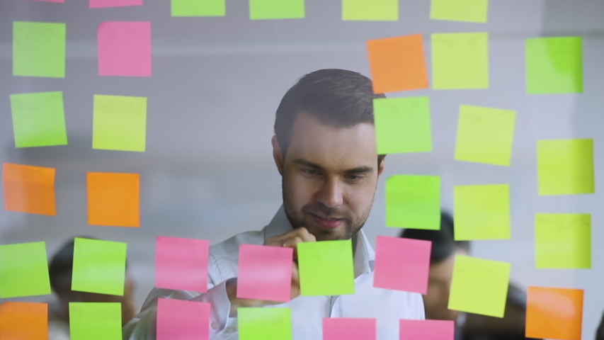 Male corporate leader scrum master write new project tasks on post it sticky notes put reminders planning work organization developing strategy attaching replacing stickers on glass board in office Royalty-Free Stock Footage #1034587574