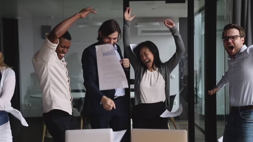 Happy successful multinational business team people dancing tossing papers celebrate success at corporate party, overjoyed excited motivated diverse colleagues group enjoy victory dance in office
