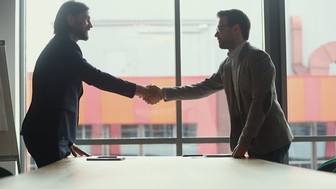 Two businessmen negotiators wear suits shake hands after successful negotiations, seller banker handshake partner client investor make investment partnership deal agreement trust concept, side view