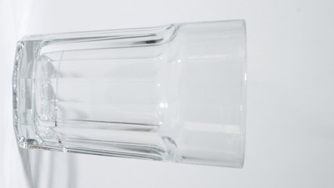 
CLOSE UP Shot Filling a transparent glass with cold water from a bottle on white background. 4k vertical shot and 30p. Pouring soda water in drinking glass, refreshing fizzy sparkling mineral liquid.