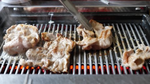 Close up view of using tong pinch a piece of Korean BBQ grilled pork meats on Electric Grill Griddle.