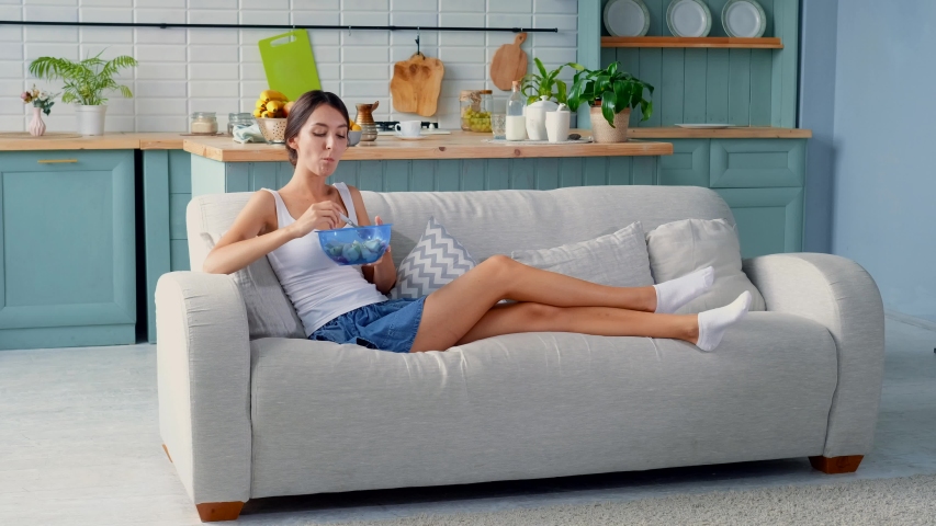 Girl eating fruit salad sitting on sofa | Shutterstock HD Video #1034602736