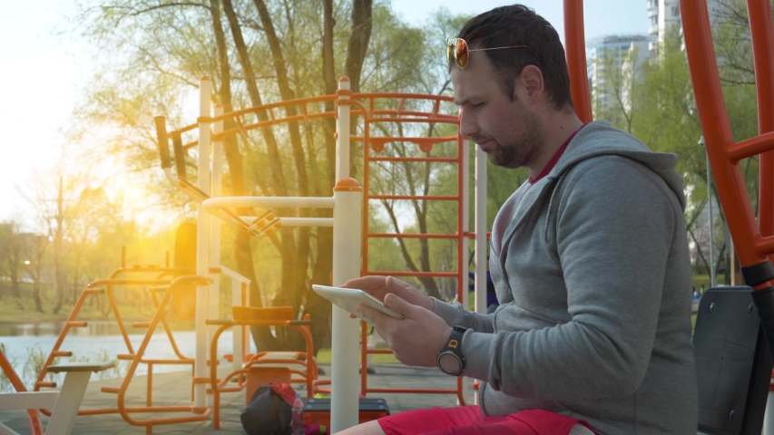 Sportsman uses tablet computer at sport ground, beautiful sun at background
