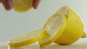 in the video we see a lemon, it is cut into slices, the hand holds one of the slices at the top and its juice drips on the other slices, white background
