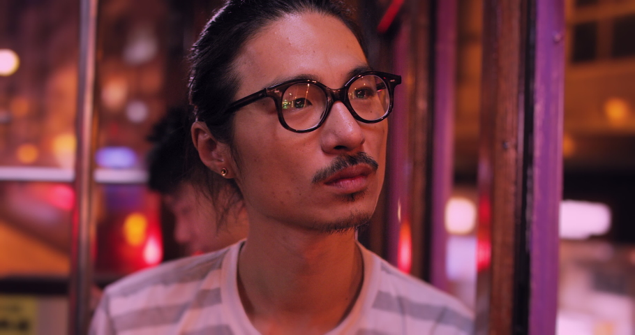 Young chinese man looking out window at city at night on Hong kong tram. Slow motion, shot on red, hand held. 