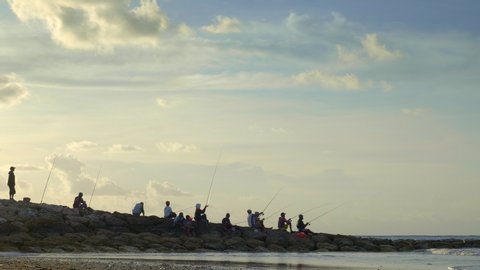Indonesian fishermen on dam with rodes during sunset