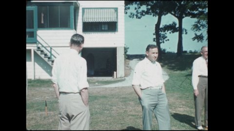 1930s: Men stand around in back yard behind house. Bald man with pipe smiles, shakes hands. Two men pick up horseshoes off ground. Man squats and waters garden, stands, picks up hose, walks.