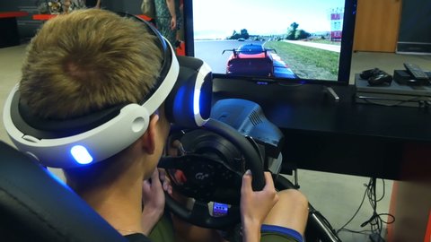 Chelyabinsk, Chelyabinsk region / Russia - 07.10.2019: Racing simulator with a steering wheel.
Boy sits in chair of virtual racer and controls sports car in the game. Virtual reality glasses is on him