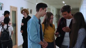 Group of teen students standing in circle watching videos together in school corridor. School friends talking together spending leisure time during a break.