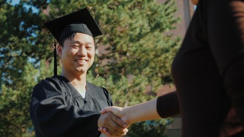 Successful Asian man in graduate clothes accepts congratulations. They shake his hand Video stock