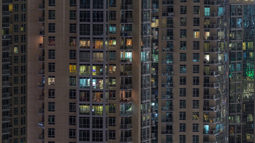 Windows of the multi-storey building with lighting inside and moving people in apartments timelapse. Aerial view of modern residential skyscrapers in Dubai downtown. Zoom in | Shutterstock HD Video #1034630705