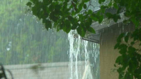 Rain flows from a house roof into a gutter during rain. close-up