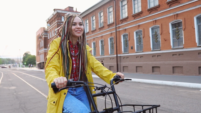 Stylish hipster girl with dreadlocks riding yellow retro bicycle in the city
