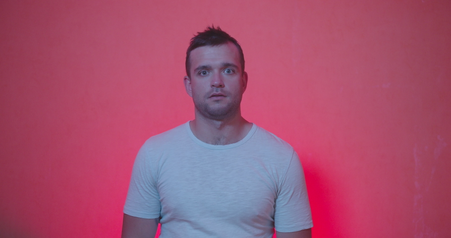 Portrait of Handsome man in white t-shirt staying from of camera and acting emotions of shocked , happiness , surprised face, clap and smiling on red and rose background , slow motion shot. 