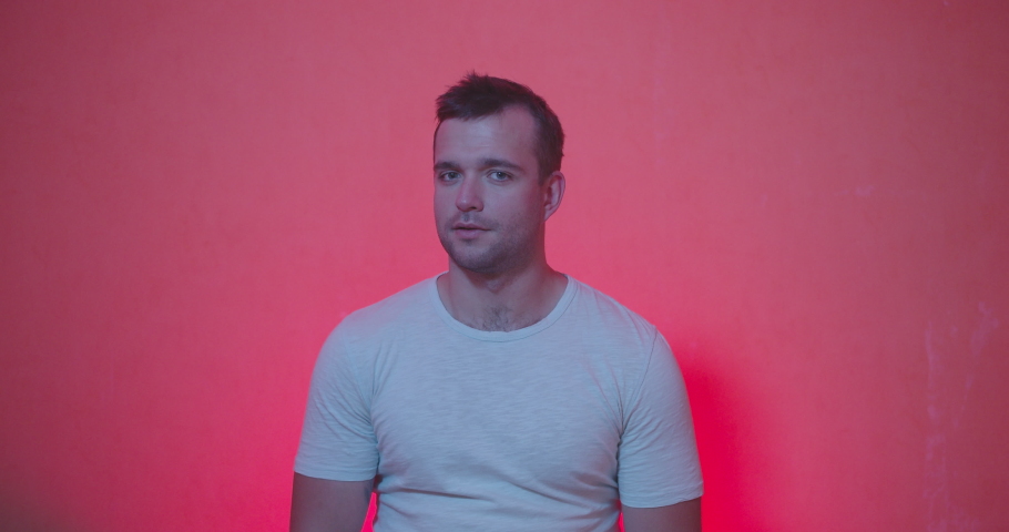 Portrait of Handsome man in white t-shirt staying from of camera and acting emotions of shocked , happiness , surprised face, clap and smiling on red and rose background , slow motion shot. 