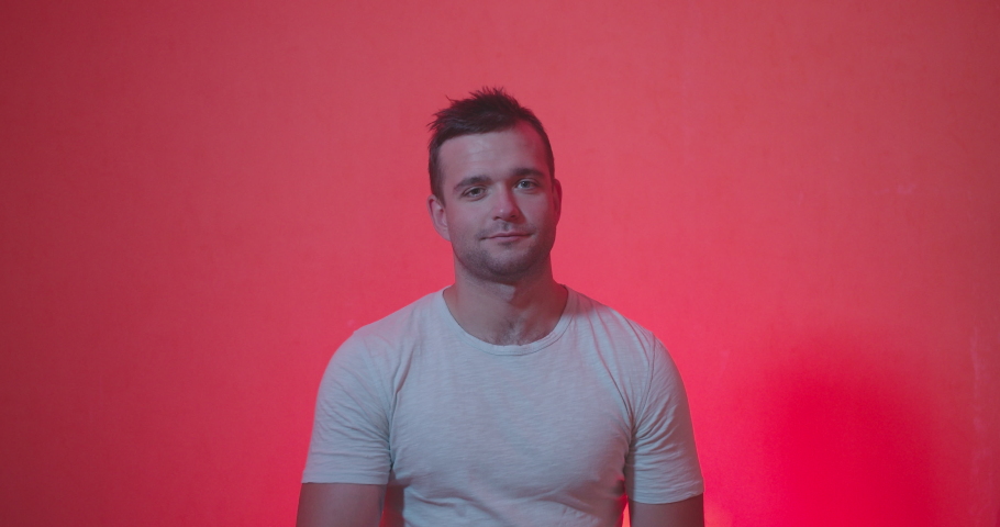 Portrait of Handsome man in white t-shirt staying from of camera and acting emotions of shocked , happiness , surprised face, clap and smiling on red and rose background , slow motion shot. 