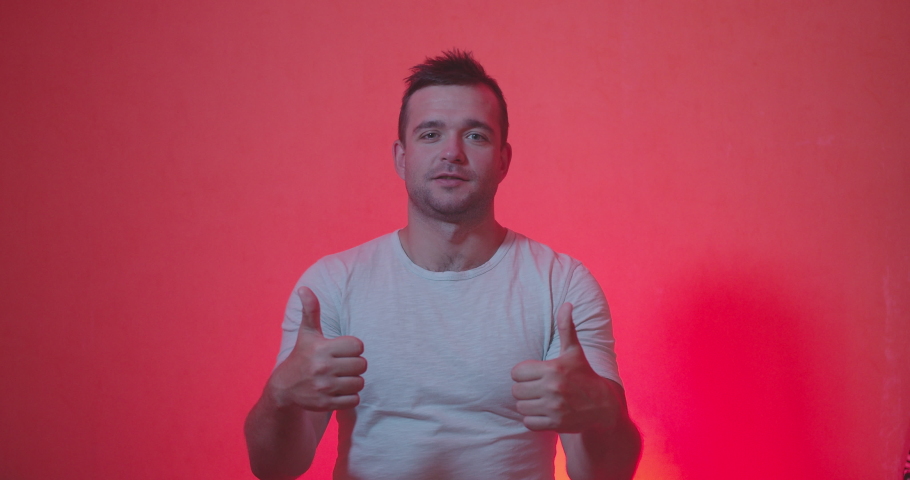 Portrait of Handsome man in white t-shirt staying from of camera and acting emotions of shocked , happiness , surprised face, clap and smiling on red and rose background , slow motion shot. 