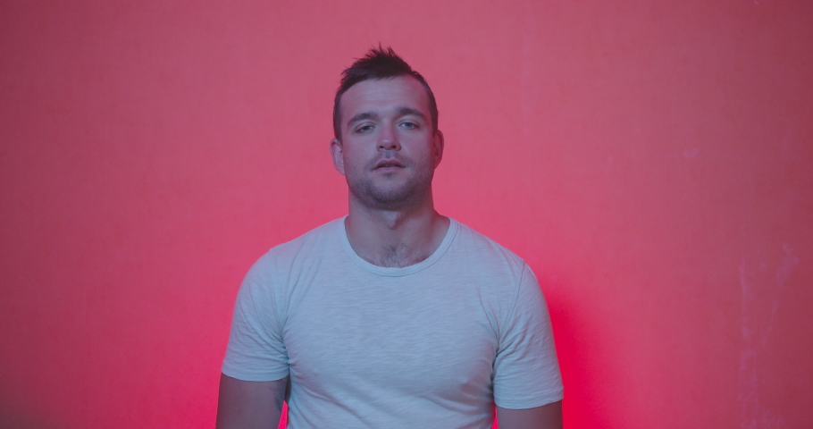Portrait of Handsome man in white t-shirt staying from of camera and acting emotions of shocked , happiness , surprised face, clap and smiling on red and rose background , slow motion shot. 