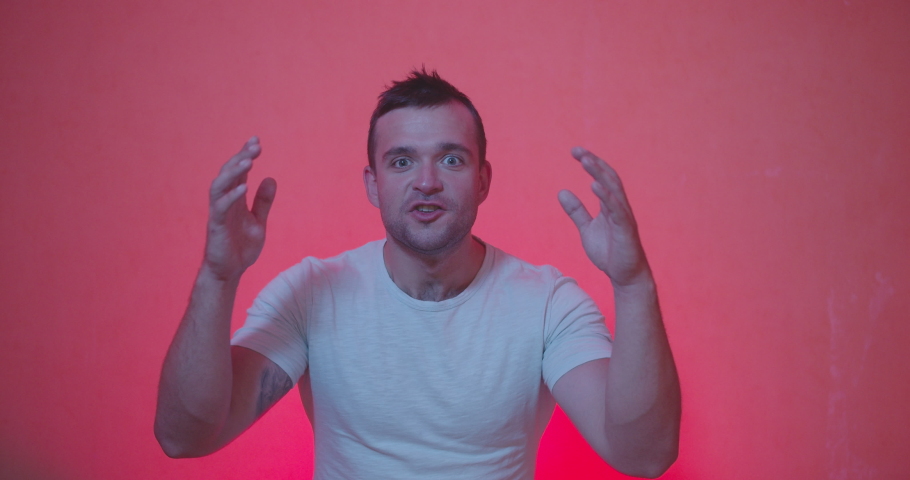 Portrait of Handsome man in white t-shirt staying from of camera and acting emotions of shocked , happiness , surprised face, clap and smiling on red and rose background , slow motion shot. 