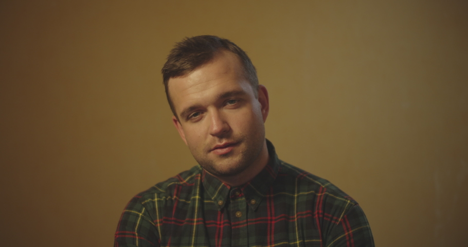 Portrait of handsome man on brown background staying front of camera and looking  with some emotions in dark shirt